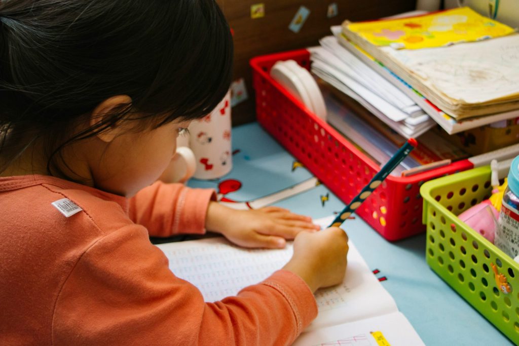 girl in orange long sleeve shirt writing on white paper